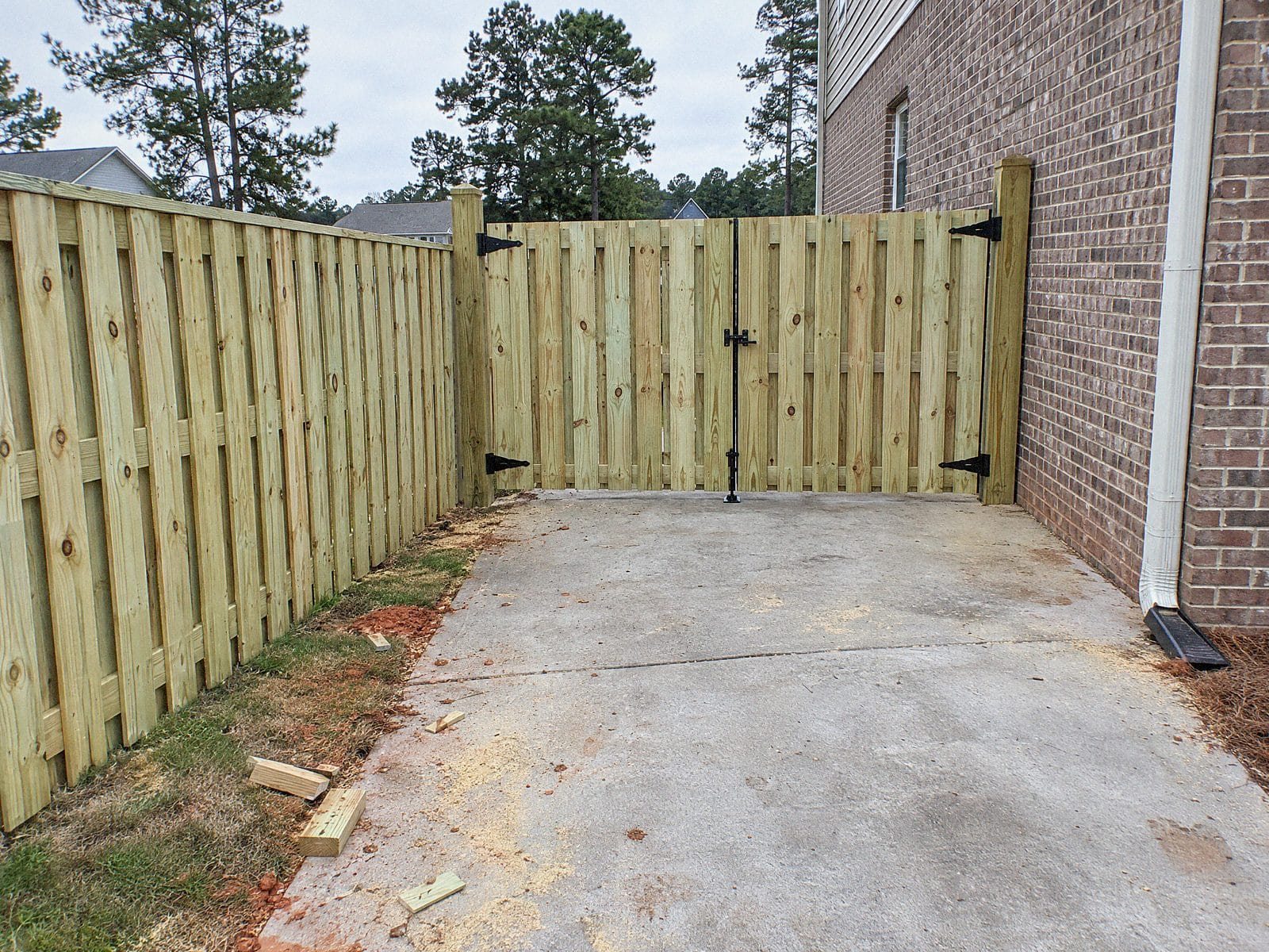 Shadowbox wood fence with a wide double gate across the end of a concrete driveway beside a brick house