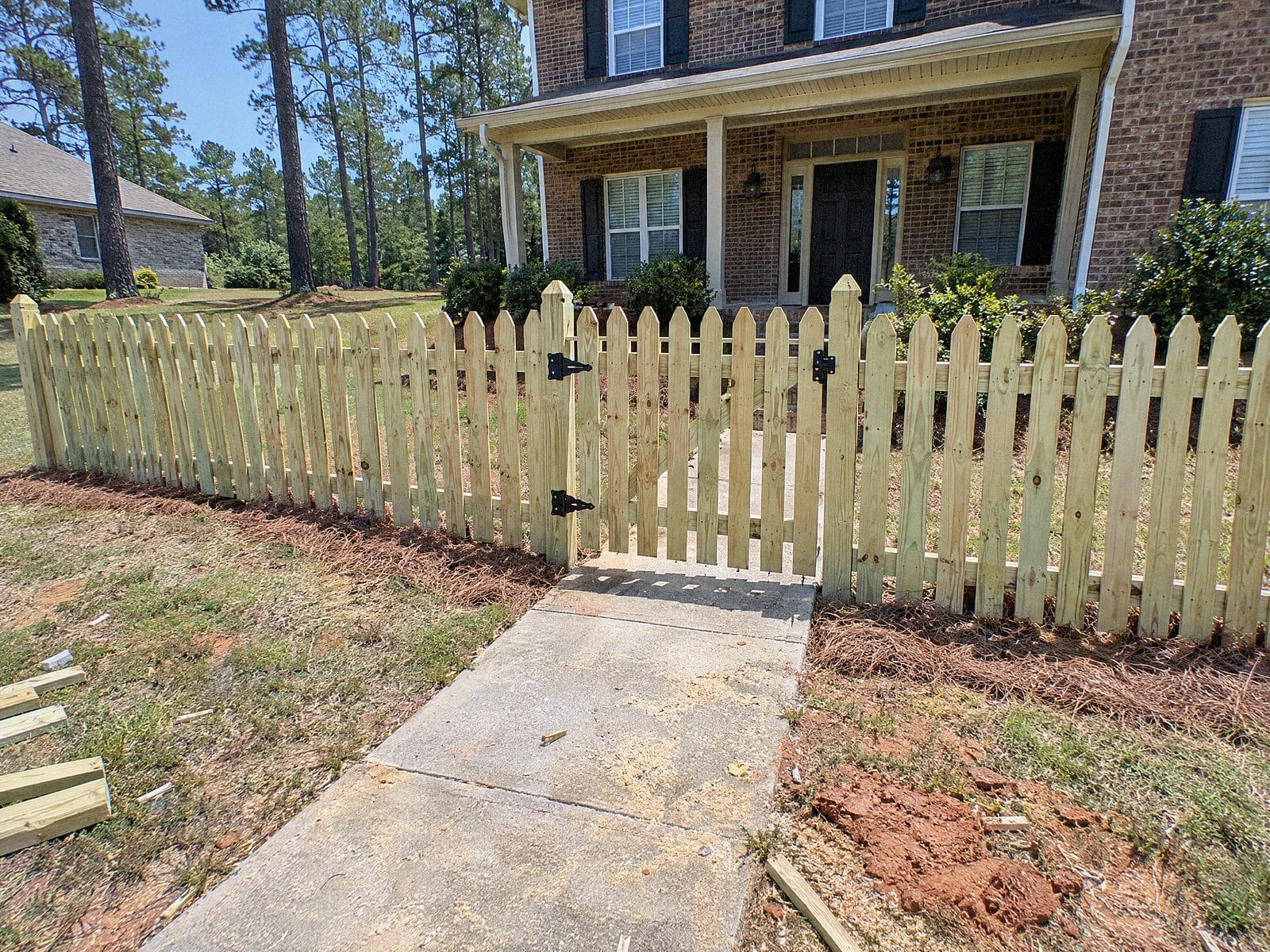 Natural wood picket fence with a walk gate across a front walkway to a brick house